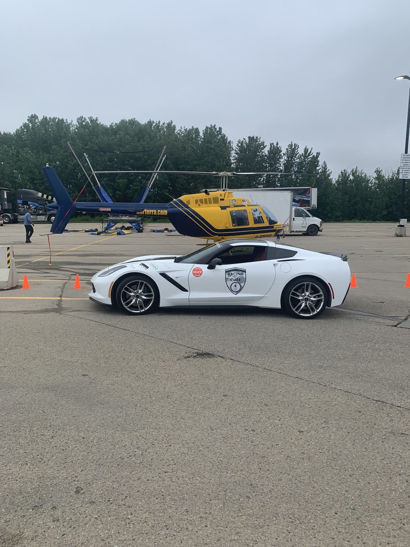 A white Corvette with a Racing for a Cure decal parked in front of a rescue helicopter on display.