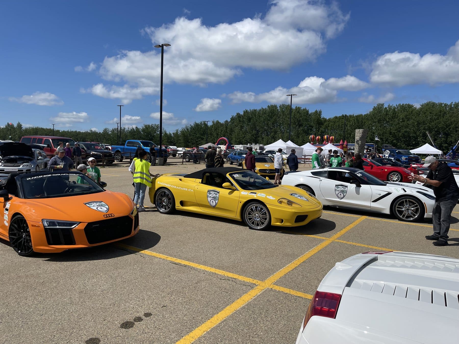 Supercars parked in a row under a blue prairie sky with event tents in the background.