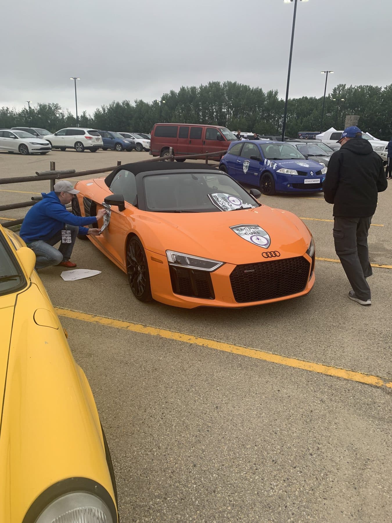 Volunteers detailing an orange Audi R8 before giving rides at a Racing for a Cure event.