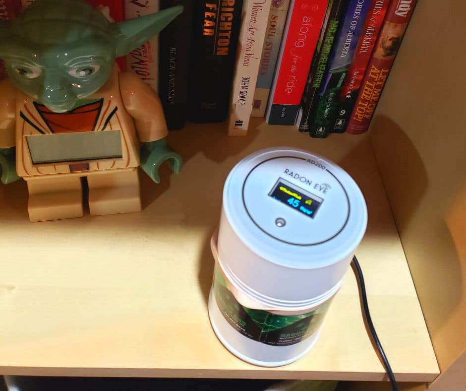 A continuous radon monitor showing a live reading, placed on a shelf in a home.